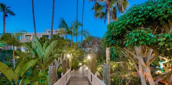 Un pont en bois mène à un bâtiment moderne, lui-même entouré d’une végétation tropicale luxuriante.