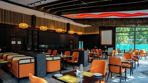 Un restaurante moderno con asientos color naranja, una zona de bar y amplios ventanales que ofrecen vistas al exterior.