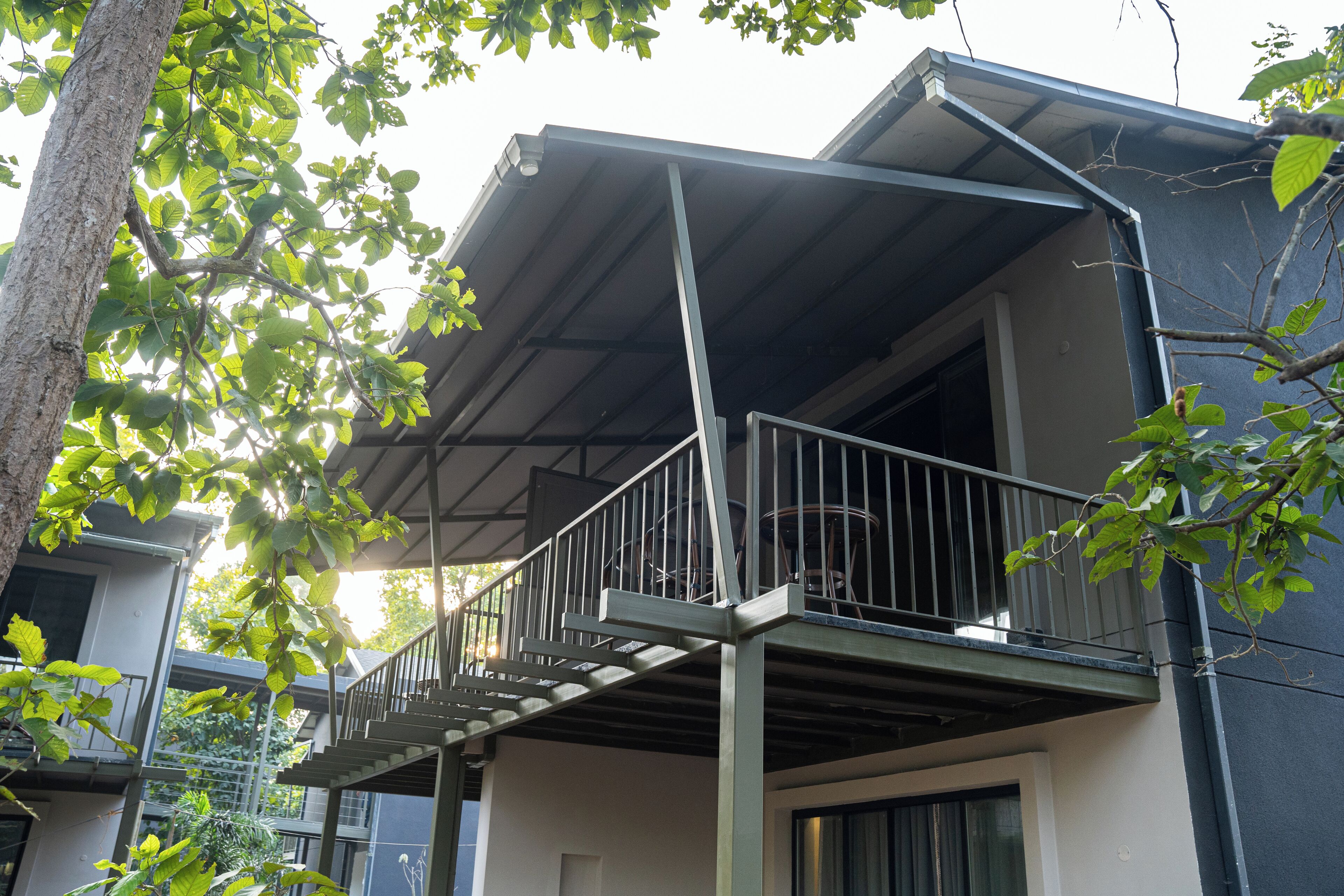 A residential building with a balcony, a staircase, and a tree in the foreground.