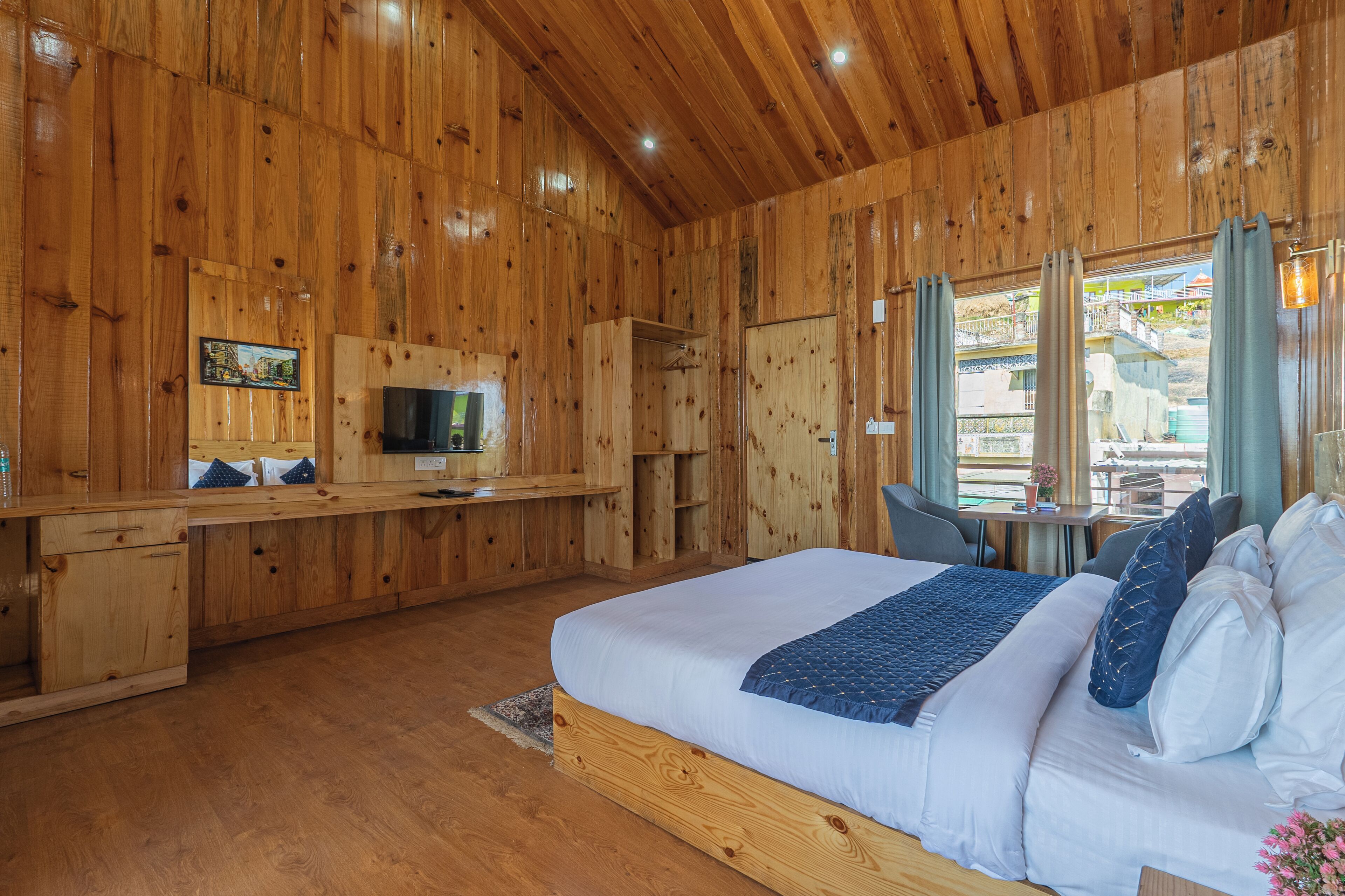 A wooden cabin-style bedroom with a bed, a TV, a desk, and a window with curtains.