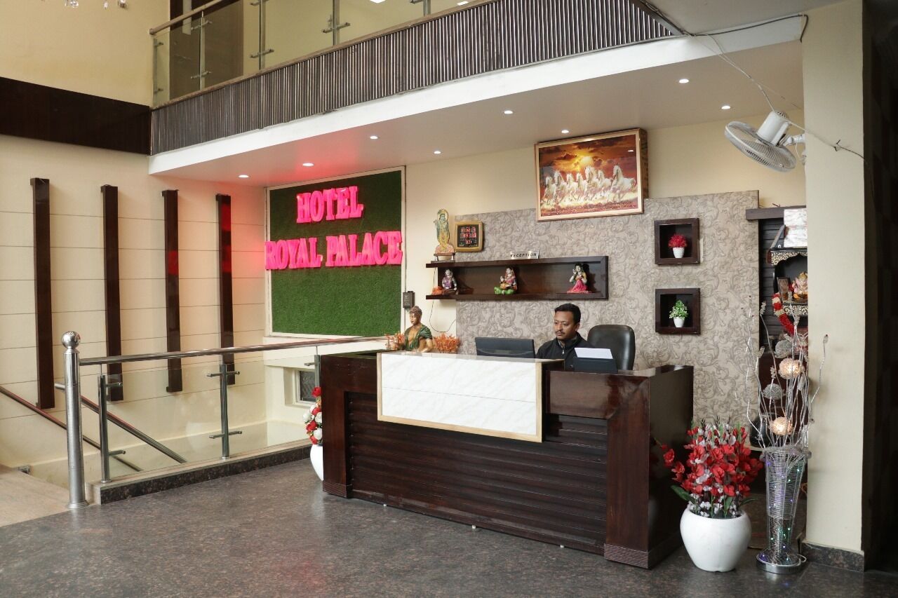 A hotel reception desk with a green sign, a reception area, a staircase, and decorative items.