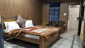 A hotel room with a wooden bed, a small table, two chairs, a blue curtain, and a wooden door. - Hotel Royal Palace Jalandhar (Jalandhar)