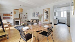 Amplia sala de estar con una mesa de comedor de madera, sillas negras, una chimenea y una cocina al fondo.