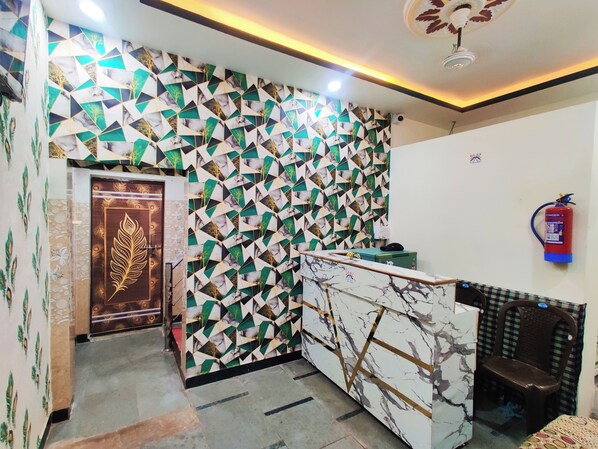 A reception area with a geometric patterned wall, a marble reception desk, a fire extinguisher, and a door with a leaf design.
