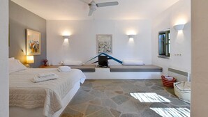 A modern hotel room with a bed, a seating area with cushions, a ceiling fan, and artwork on the walls.