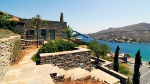 A stone house with a stone staircase leading to a terrace overlooking a body of water and hills.