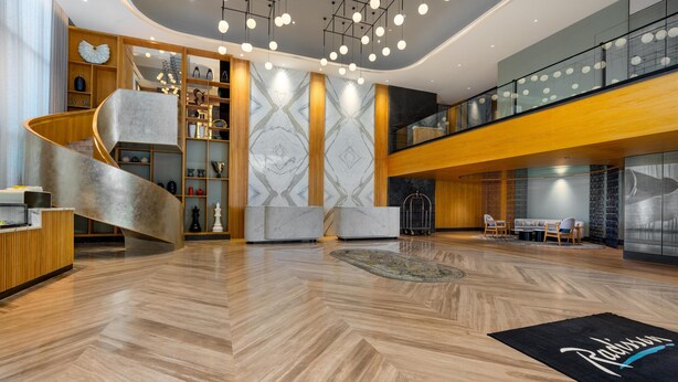 Eine moderne Hotelhalle mit einer geschwungenen Treppe, einem Holzbüro für die Rezeption und einer großen Wand mit Muster.