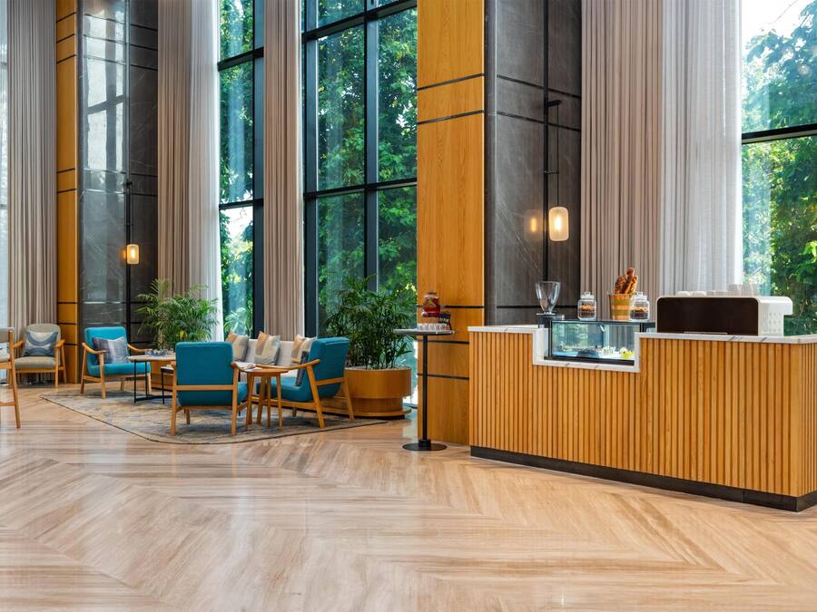 A modern reception area with a wooden counter, seating area with blue chairs, and large windows offering a view of greenery.