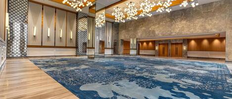 A spacious lobby with a patterned carpet, wooden flooring, and a modern chandelier.
