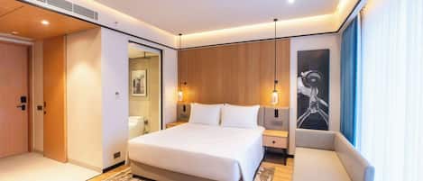 A modern hotel room with a large bed, a sofa, a wooden panel wall, and a large window with curtains.