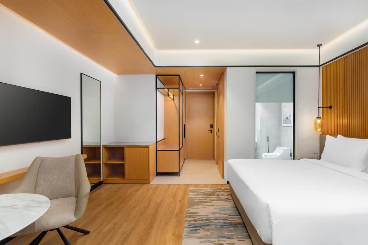 A modern hotel room with a large bed, a desk, a chair, and a television.