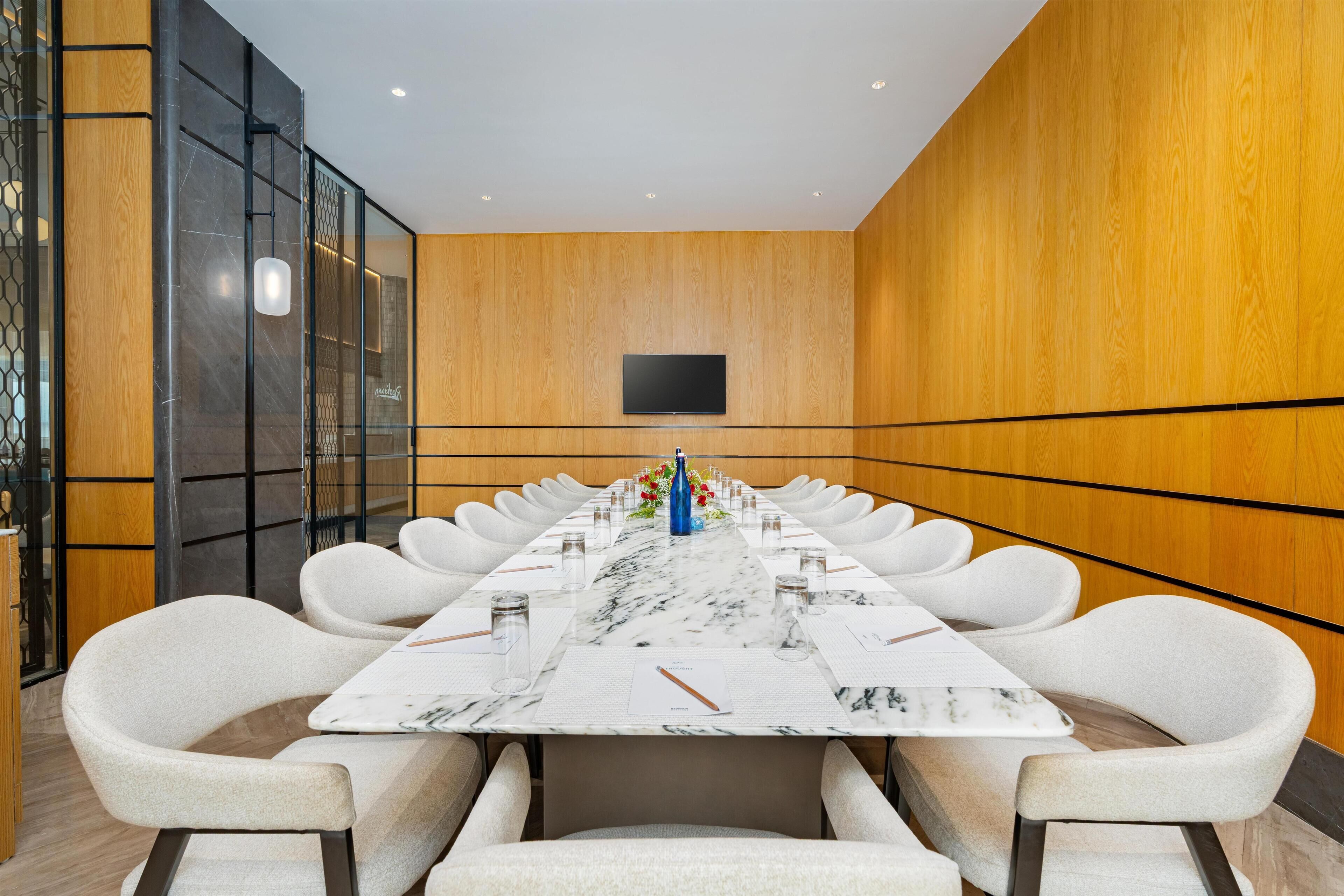 A conference room with a long table, white chairs, and a flat-screen TV on the wall.