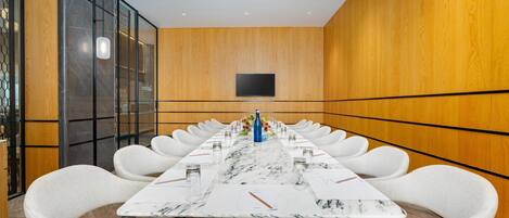 A conference room with a long table, white chairs, and a flat-screen TV on the wall.