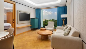 Ein modernes Hotelzimmer mit großem Fernseher, bequemen Sitzmöglichkeiten, einem Holztisch und Blick auf die Stadt.