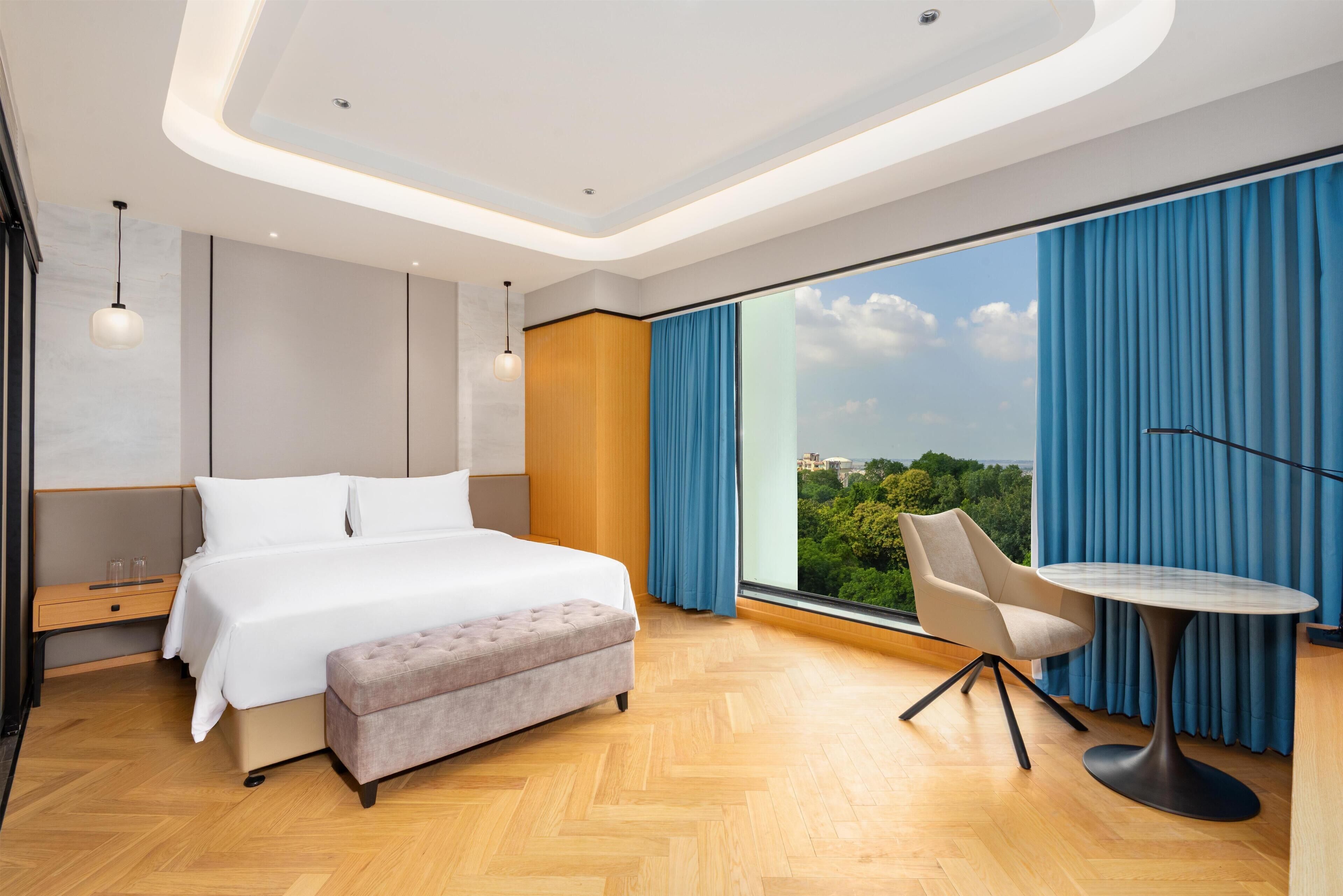Een moderne hotelkamer met een groot bed, een zithoekje en uitzicht op het groen.