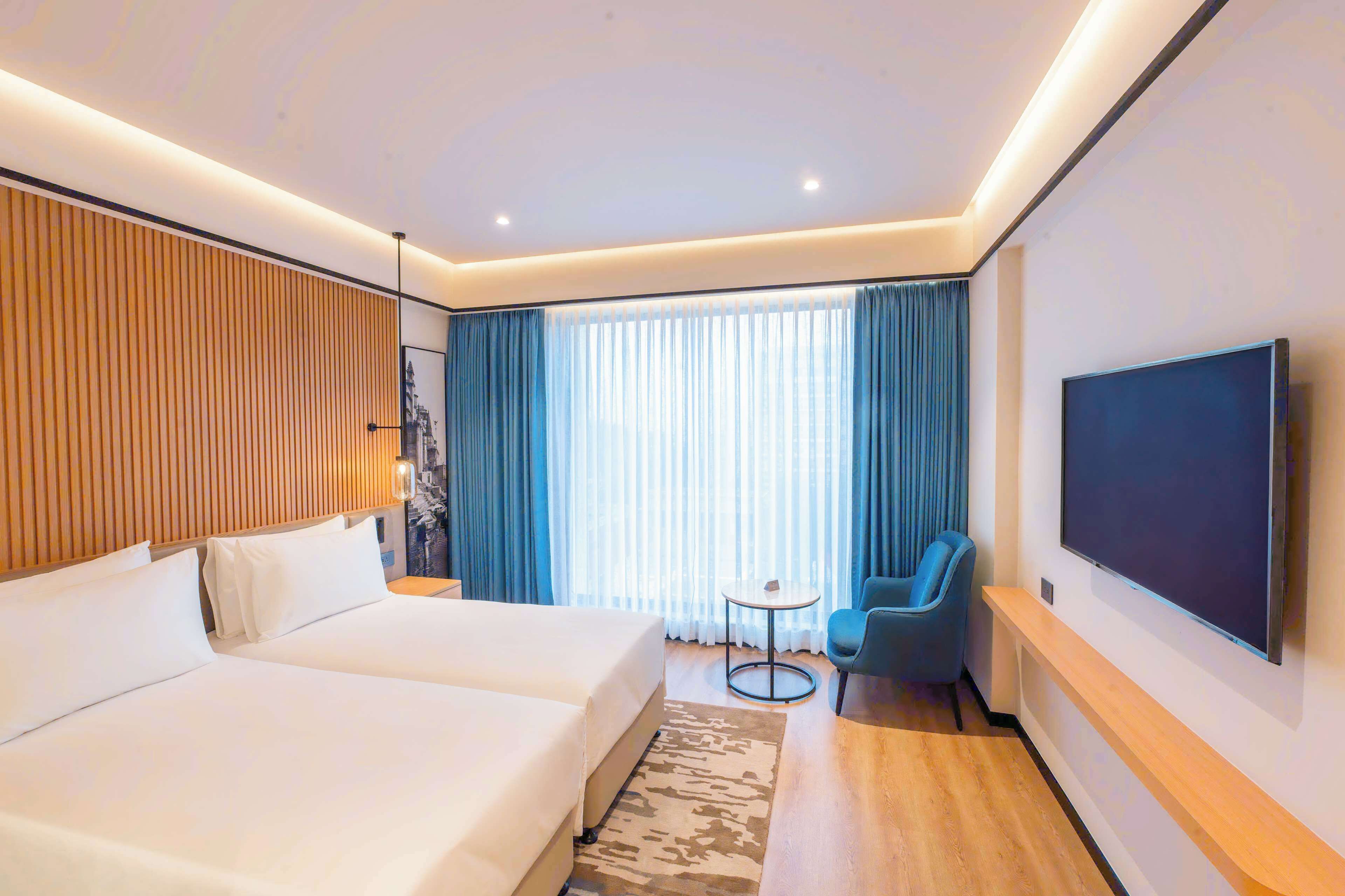 A modern hotel room with a large bed, a TV, a small table, and a chair.