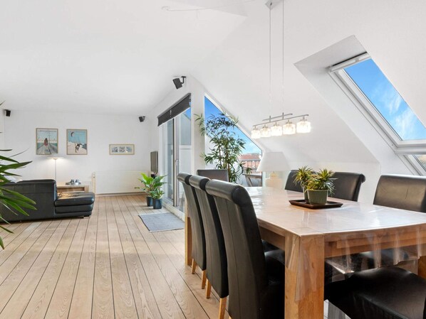 A modern dining area with a wooden table and black chairs, a large window, and a view of the sky. - 5 Star Holiday Home in Lokken (Lokken)