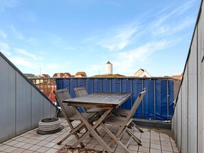 A rooftop terrace with a table and chairs, a blue safety fence, and a view of buildings and a silo in the background. - 5 Star Holiday Home in Lokken (Lokken)