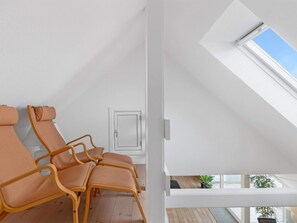 A room with a sloped ceiling, a skylight, and a view of the outdoors. There are two wooden chairs with cushions.