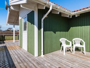 A green building with a white exterior, a wooden deck, and two white plastic chairs.