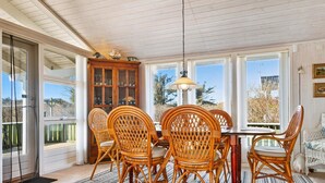 A dining area with wicker chairs, a wooden table, and a hanging light fixture.