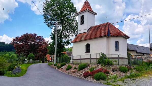 A small church with a red-tiled roof and a bell tower, surrounded by greenery and a paved road. - Villa in Bysovec Near Harusak Ski Resort (Býšovec)