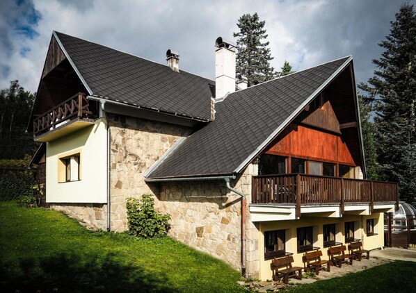 A stone building with a sloped roof, a wooden balcony, and a small garden area. - Villa in Stare Hamry Near Ski Park Grun (Staré Hamry)