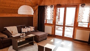 A cozy living room with a sofa, a coffee table with flowers, and a fireplace. - Villa in Stare Hamry Near Ski Park Grun (Staré Hamry)
