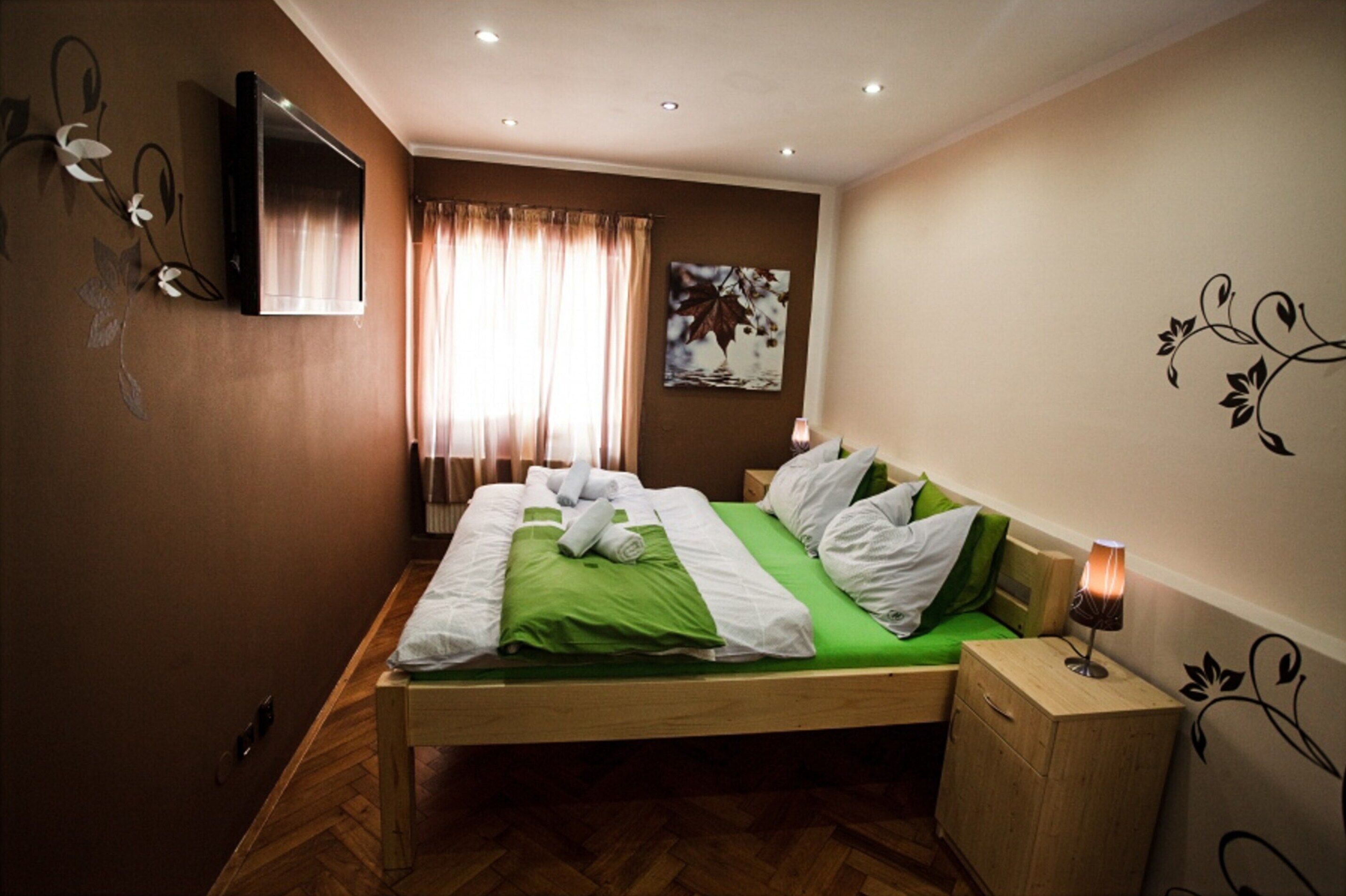 Una cama bien hecha con ropa de cama verde y blanca, una mesita de noche con lámpara y un televisor montado en la pared.