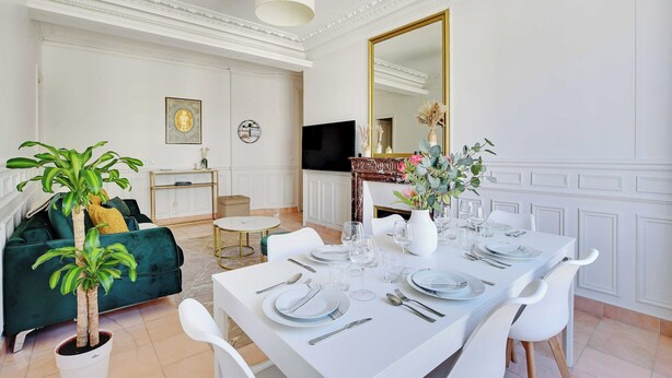 A dining area with a white table set for four, a green sofa, and a potted plant. - Modern Apartment - 2bd/4p - Louvre/marais (Paris)