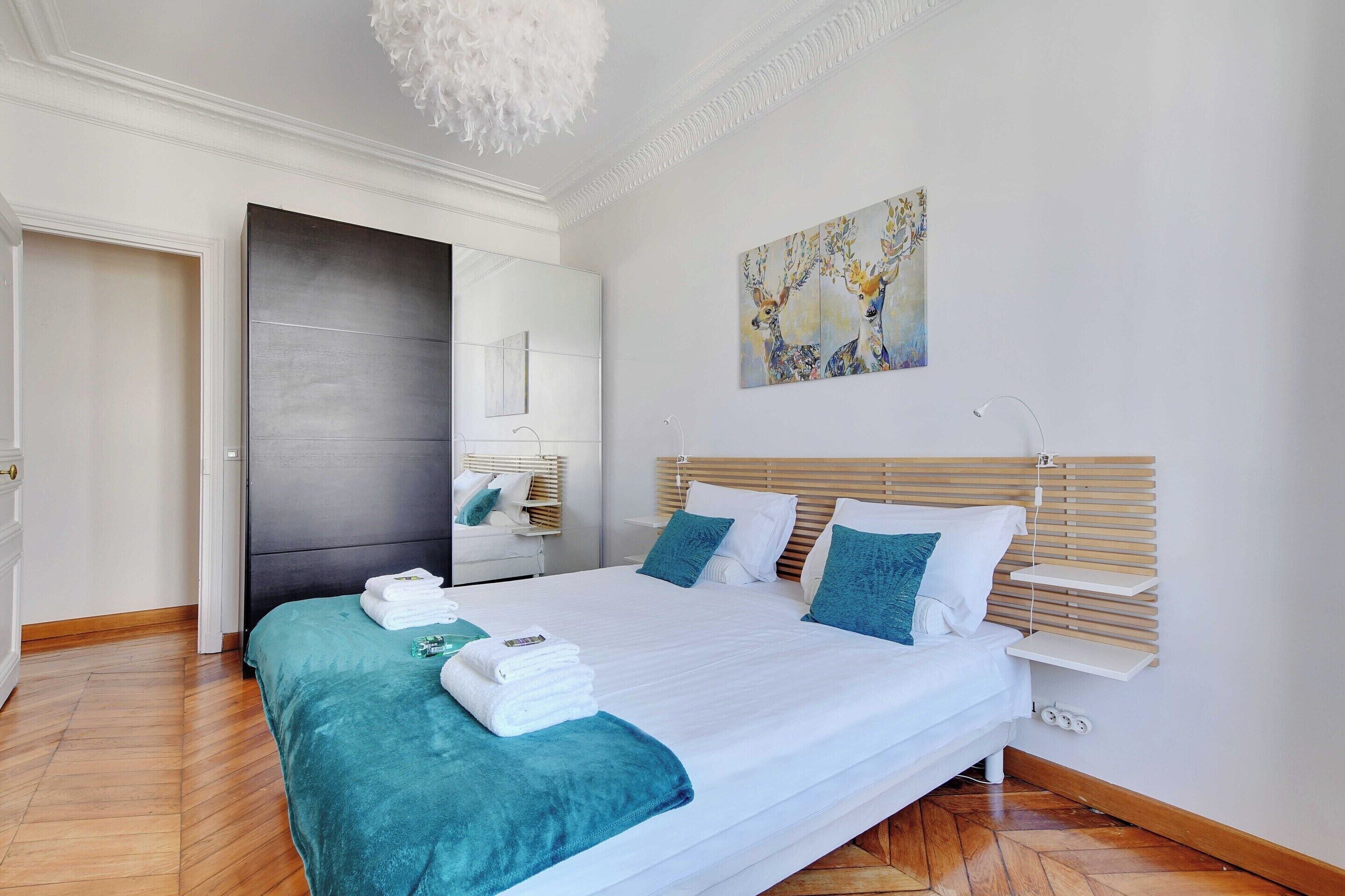 A modern bedroom with a large bed, a wooden floor, a white wall, and a painting of deer.