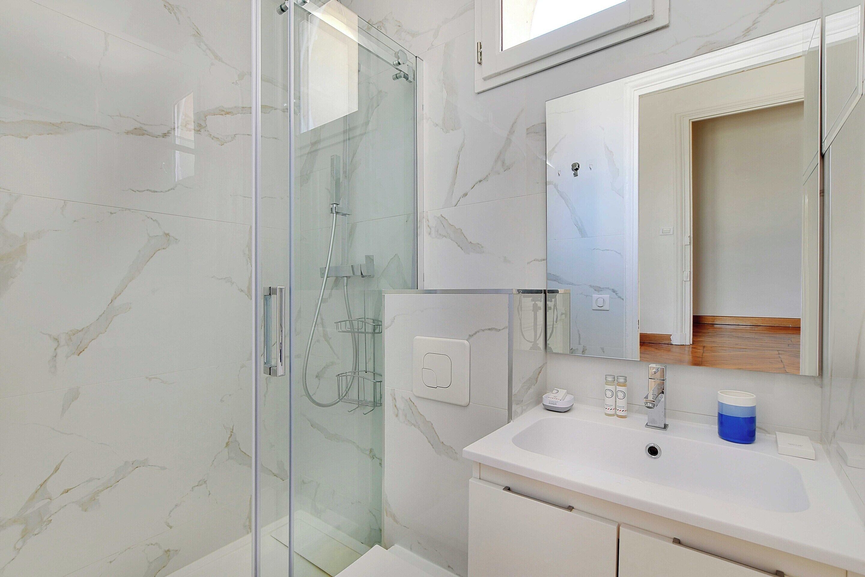 A modern bathroom with a glass shower enclosure, a white sink, and a mirror above it.