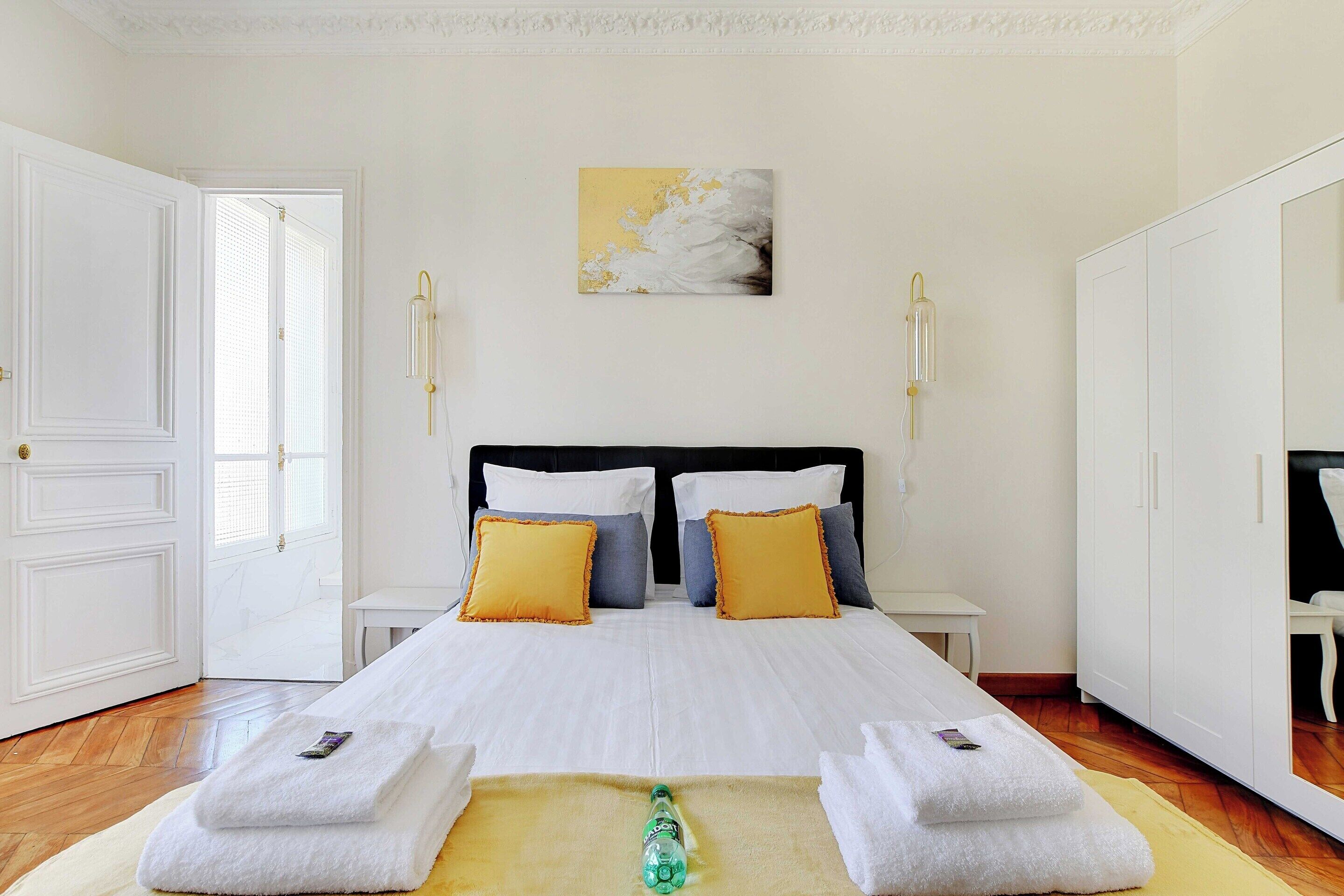 A hotel room with a large bed, white walls, a painting, and a wardrobe.