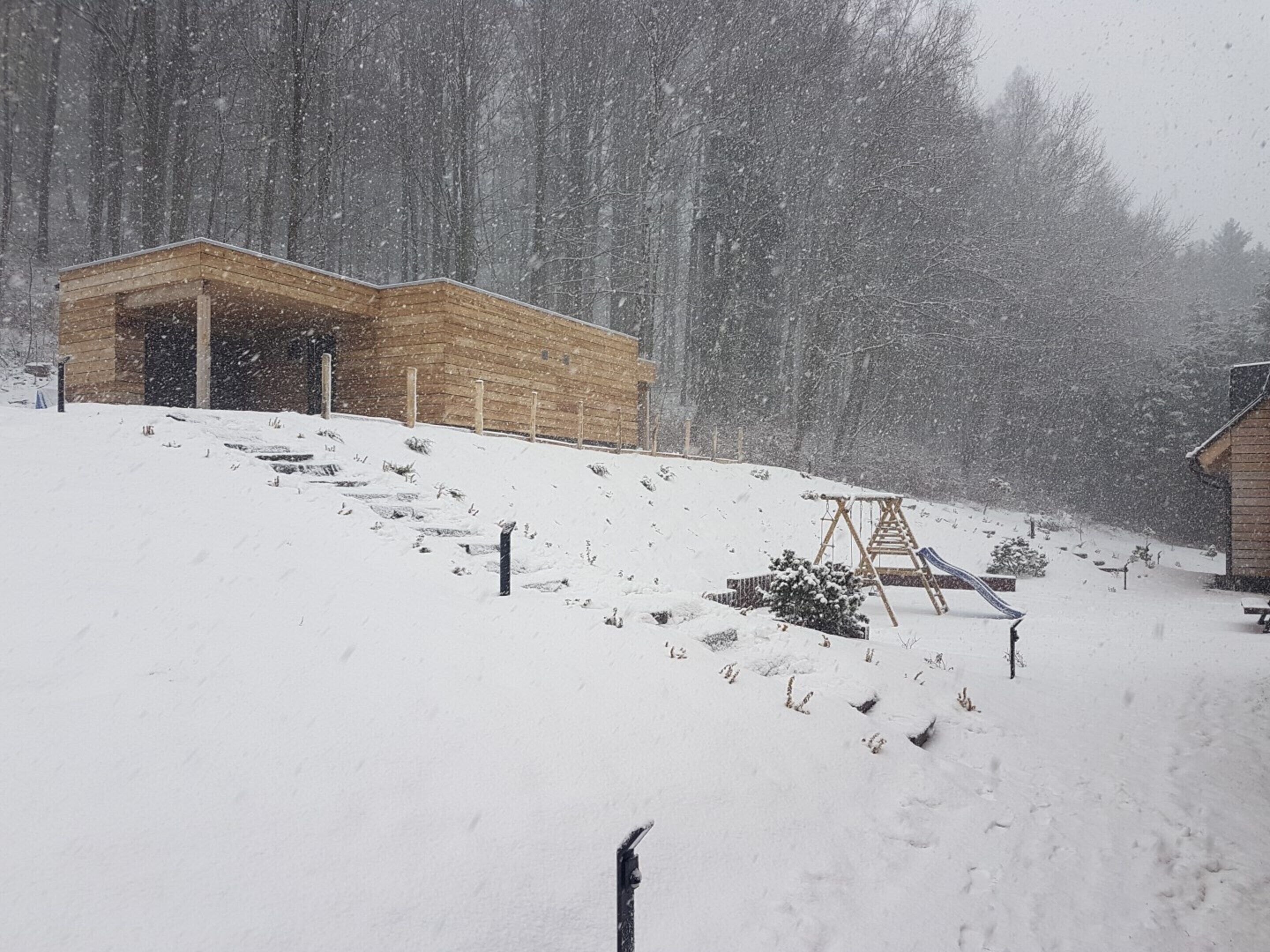 A wooden cabin with a porch, surrounded by a snowy landscape and a forest.