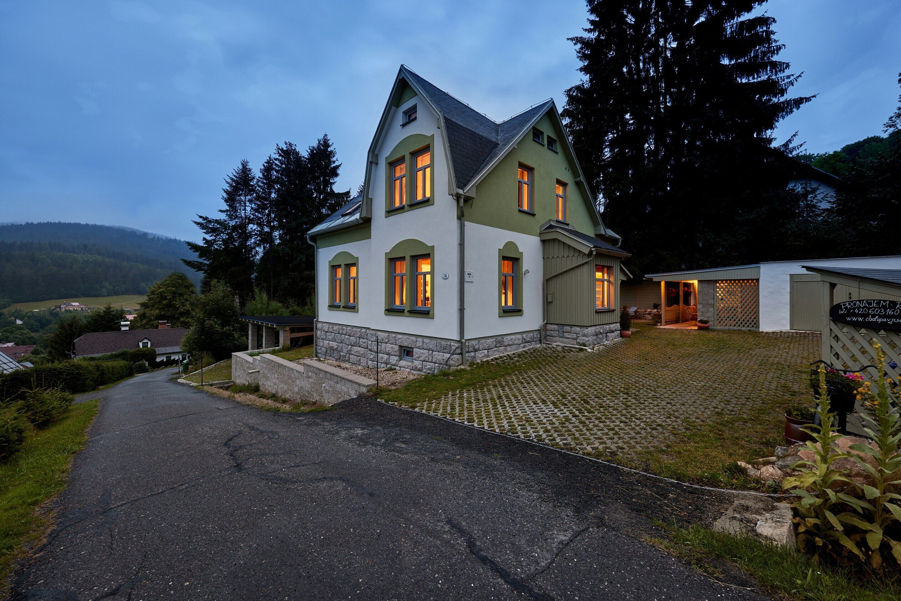 Une maison à deux étages, avec des fondations en pierre, un toit en pente et une allée pavée menant à l’entrée.