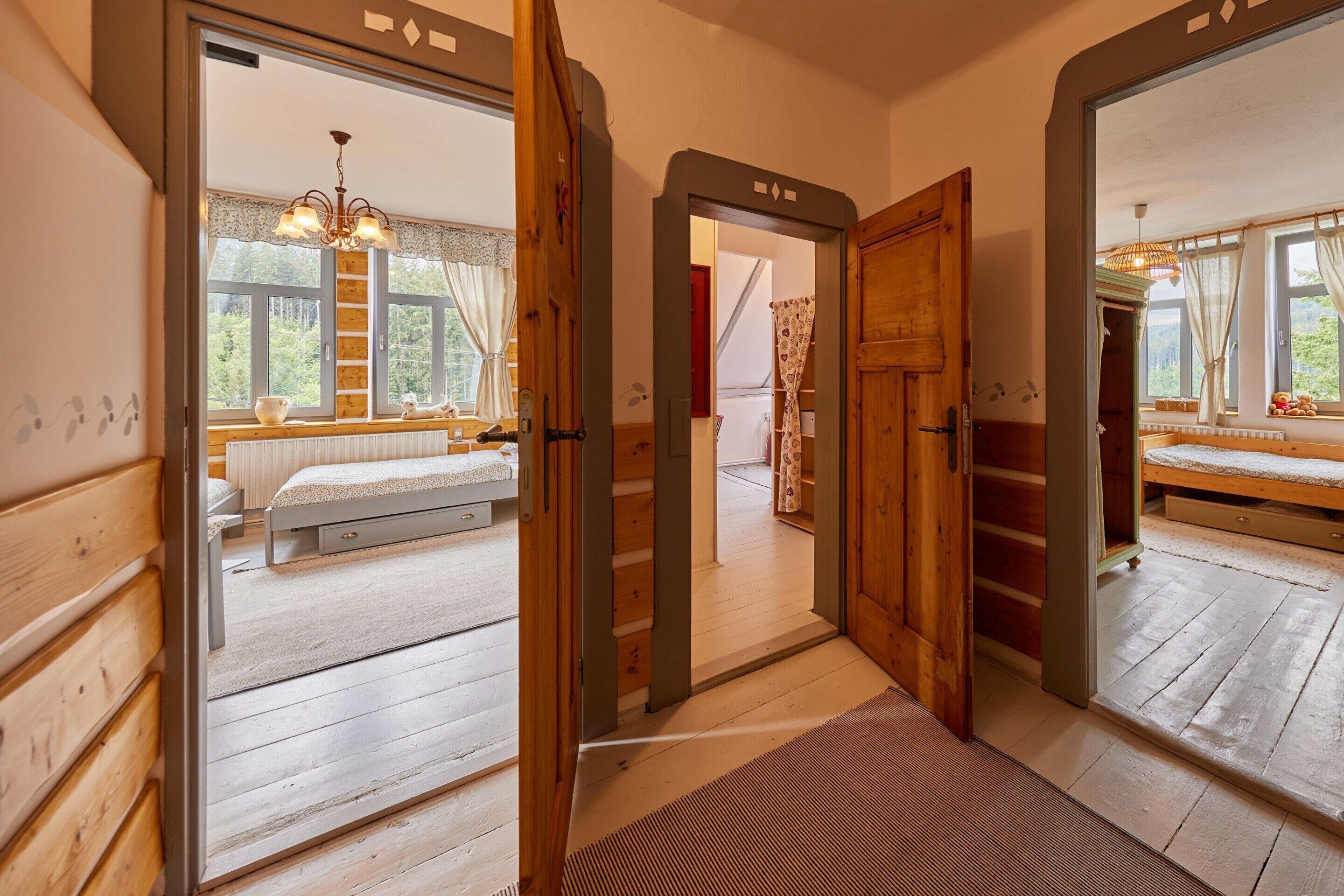 A wooden interior with a bed, a mirror, and a view of a room with a window and a ladder.