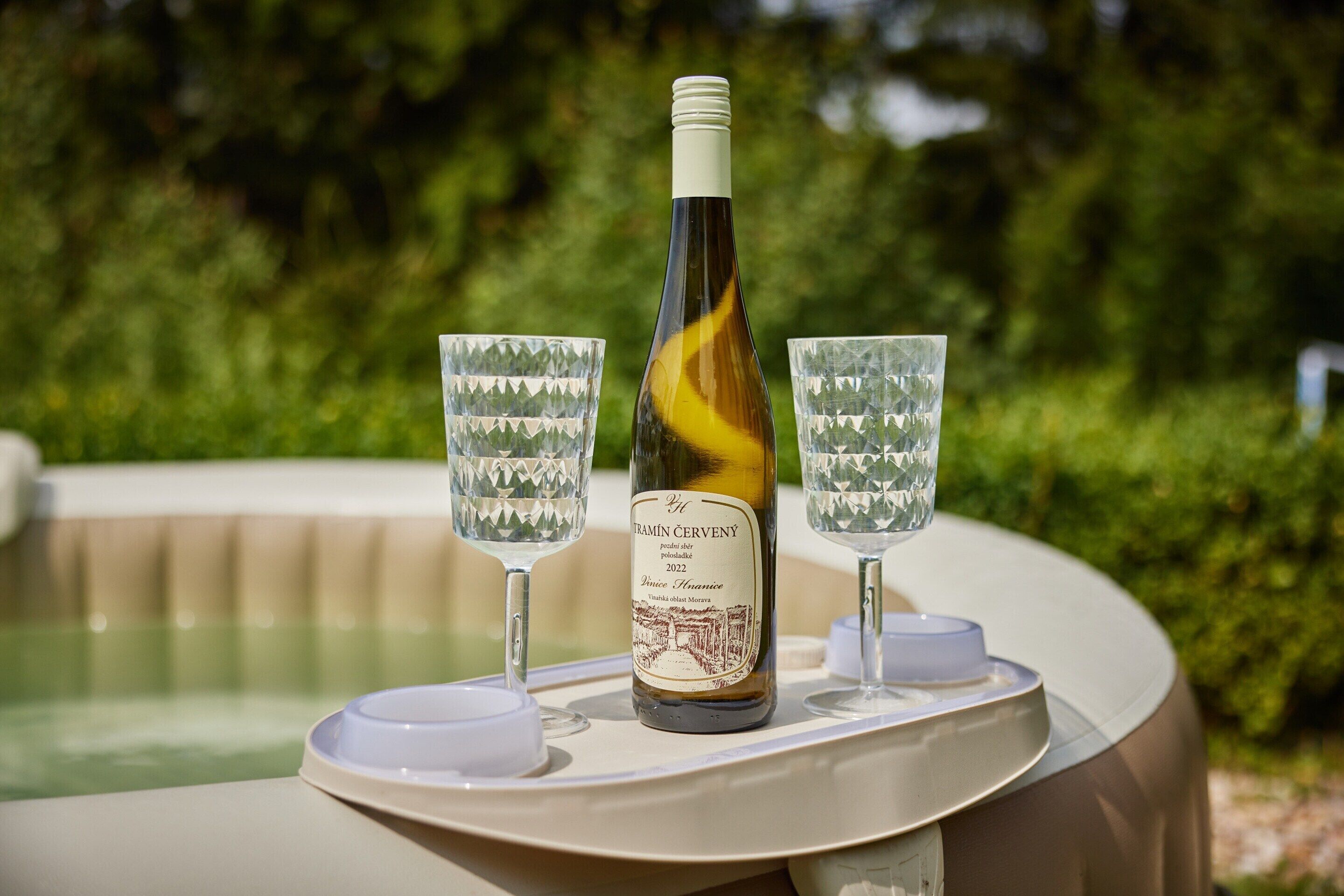A bottle of wine and two glasses on a table near a pool.