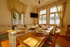 A dining room with a wooden table set for a meal, flanked by floral-patterned sofas and a television mounted on the wall.