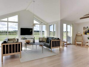 A spacious living room with a large window, a flat-screen TV, a sofa, a coffee table, and a chair. - 5 Star Holiday Home in Lokken (Lokken)