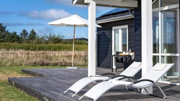 Une terrasse extérieure moderne, dotée de chaises longues et d’une table, offrant une vue sur un paysage naturel.