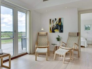 A spacious room with a large sliding glass door leading to an outdoor area, two wooden chairs, a small table with a plant, and a bed with a white bedspread. - 5 Star Holiday Home in Lokken (Lokken)