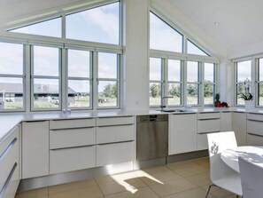 A modern kitchen with large windows, white cabinetry, and a dishwasher. - 5 Star Holiday Home in Lokken (Lokken)