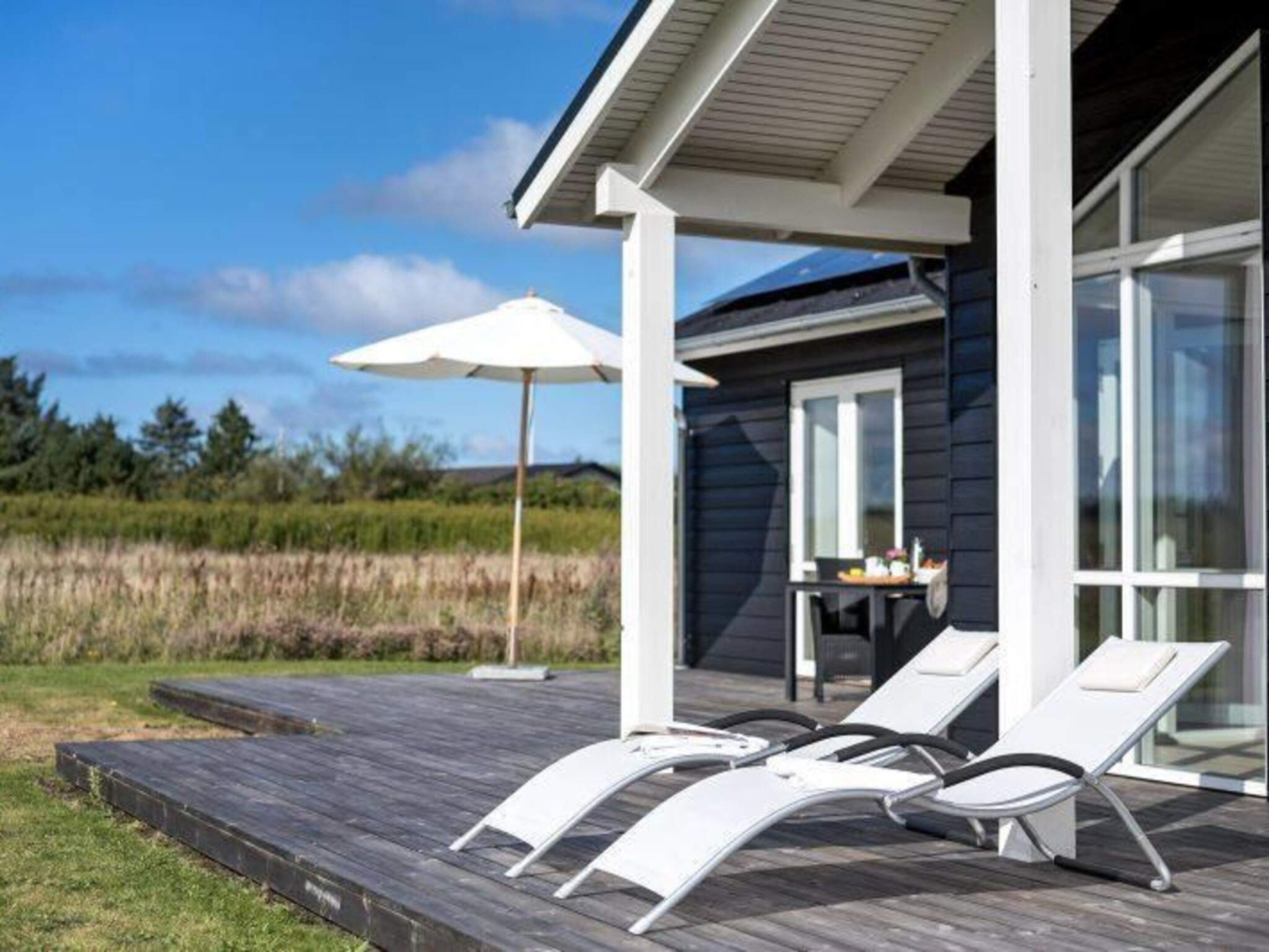 A modern outdoor deck with lounge chairs and a table, overlooking a natural landscape.
