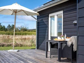 A deck with a table and chairs, an umbrella, and a window overlooking a natural landscape. - 5 Star Holiday Home in Lokken (Lokken)