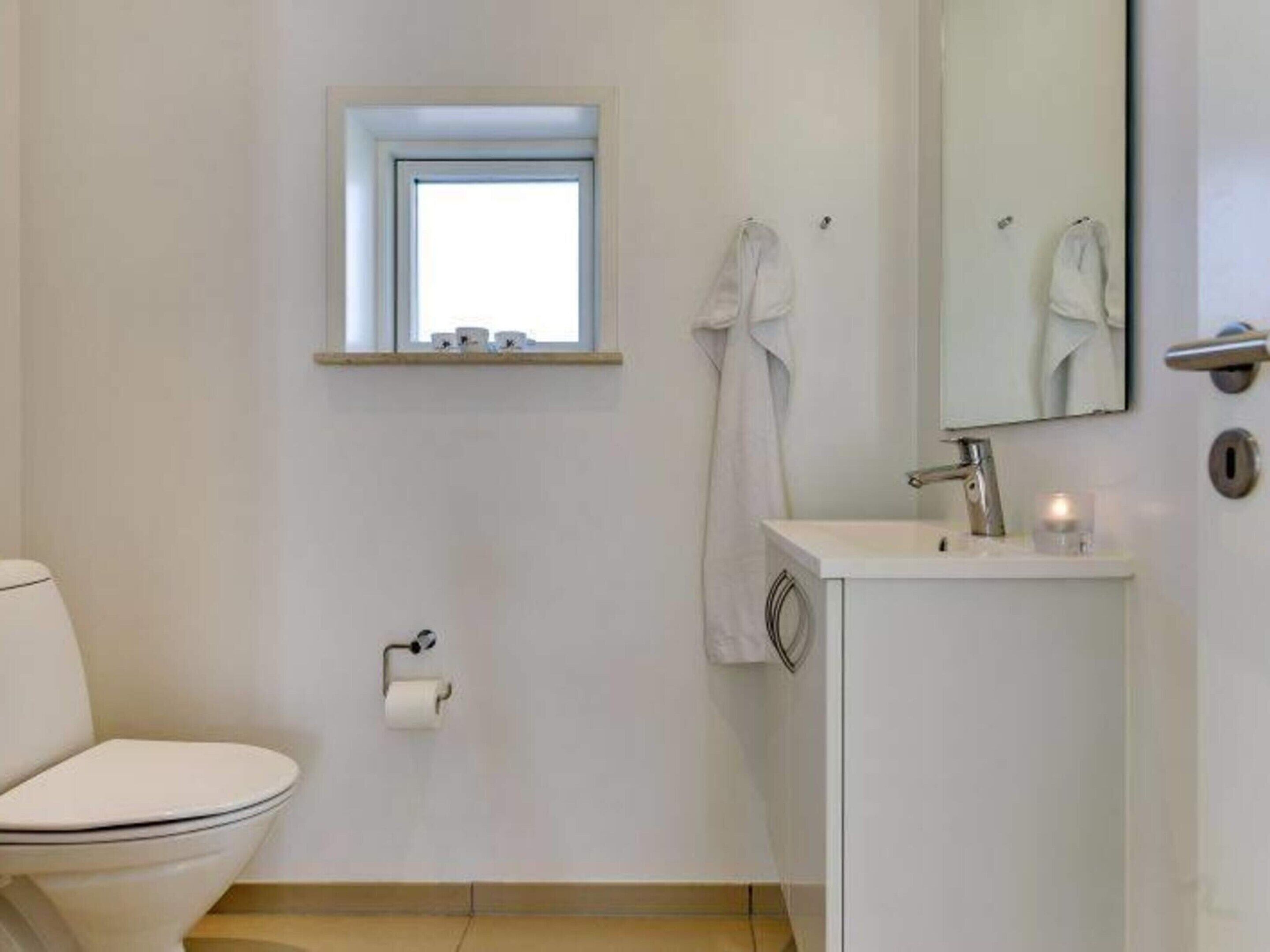 A small, clean bathroom with a toilet, a sink, a mirror, and a window.