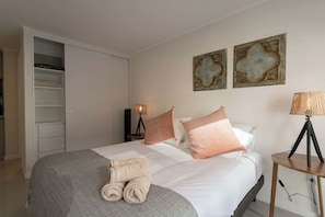 Ein ordentlich bezogenes Bett mit grauer Decke, zwei zusammengerollte Handtücher und zwei Zierkissen.