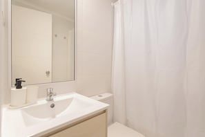 A bathroom with a white sink, mirror, toilet, and shower curtain.