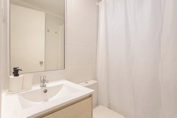 Ein Badezimmer mit weißem Waschbecken, Spiegel, Toilette und Duschvorhang.