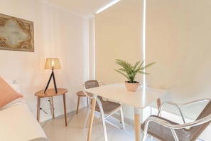 Ein modernes Zimmer mit einem weißen Tisch, Korbstühlen, einer Topfpflanze, einer Lampe und einem Bild an der Wand.