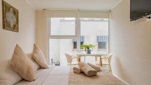 Une chambre à coucher avec un lit, des oreillers, une fenêtre, une table avec des chaises et une plante.